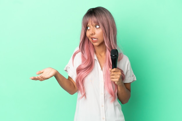 Mujer joven cantante de raza mixta con cabello rosado aislado sobre fondo verde con expresión de sorpresa mientras mira de lado