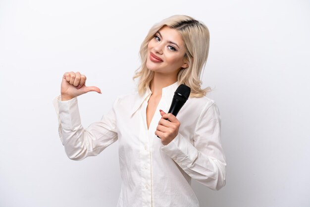 Mujer joven cantante recogiendo un micrófono aislado sobre fondo blanco orgullosa y satisfecha