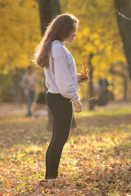 Mujer joven con capucha blanca sosteniendo hojas amarillas en el parque de otoño