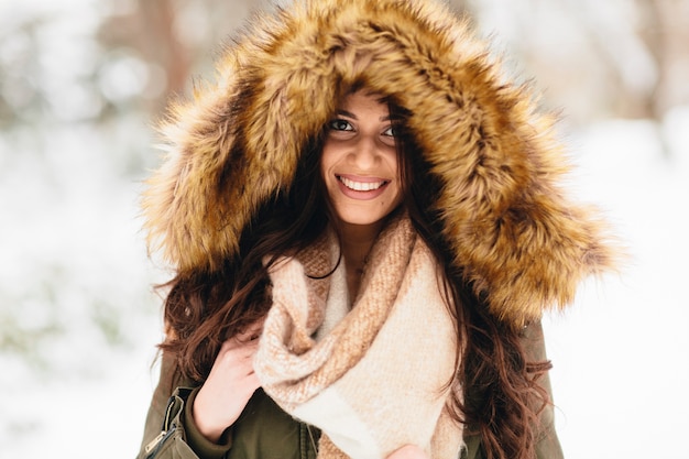 Mujer joven con una capucha de piel en el parque en la nieve.