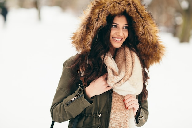 Mujer joven con una capucha de piel en el parque en la nieve.