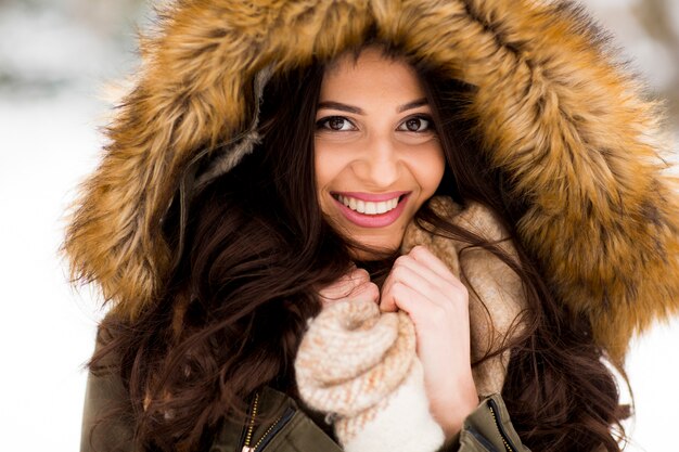 Mujer joven con una capucha de piel en el parque en la nieve.