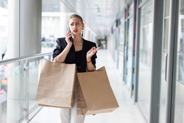 Mujer joven carismática con bolsas de compras hablando por teléfono en el centro comercial