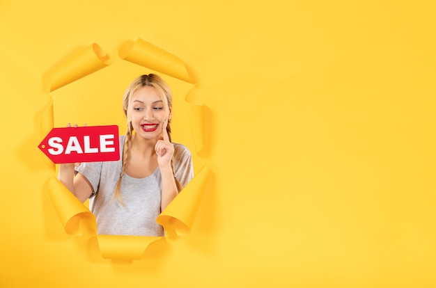 Foto mujer joven con cartel de inscripción de venta en la superficie de papel amarillo rasgado compras faciales interiores