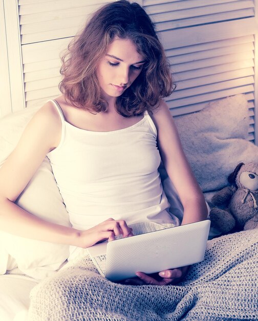 Mujer joven en casa en la cama usando una computadora portátil
