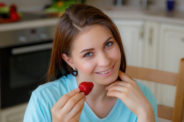 Foto mujer joven en casa en la cocina comiendo fruta