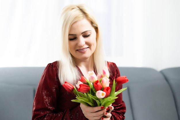 Mujer joven en casa el concepto del día de la madre con ramo de tulipanes sonriendo de cerca.