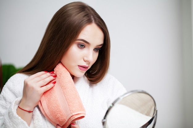 Mujer joven en casa frente a un espejo se limpia la cara después de los tratamientos de spa.