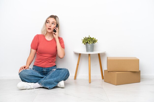 Mujer joven en casa nueva entre cajas aisladas sobre fondo blanco manteniendo una conversación con el teléfono móvil