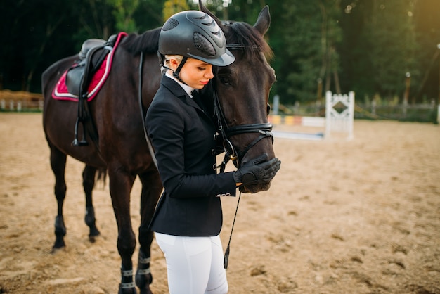 Mujer joven en casco abraza a caballo, paseos a caballo. Semental marrón, ocio con animal, deporte ecuestre