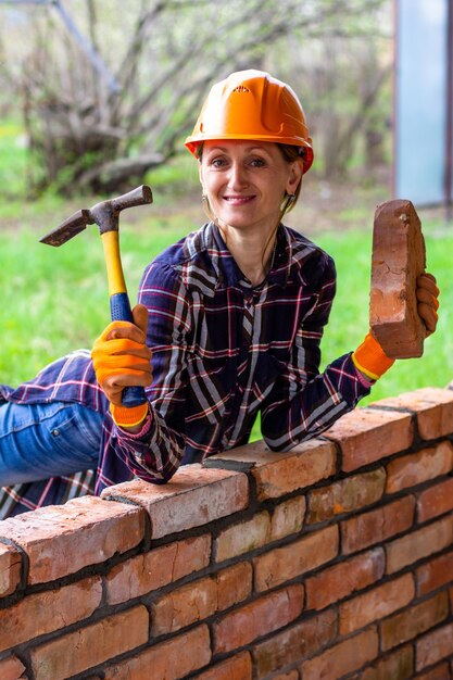 Foto una mujer joven con un casco de construcción con un martillo y un ladrillo en las manos sonríe