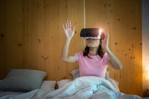 Mujer joven con casco de realidad virtual en la cama VR Futuro tecnología digital juego películas entretenimiento metaverso NFT y concepto de ciberespacio 3D