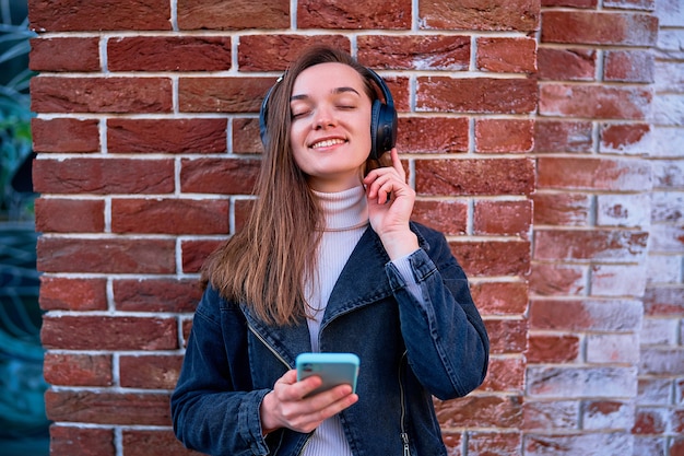 Mujer joven casual feliz sonriente moderna que usa auriculares inalámbricos y smartphone para escuchar música al aire libre