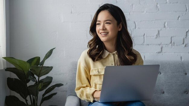 Mujer joven casual sentada sonriendo sosteniendo una computadora portátil aislada en la pared blanca