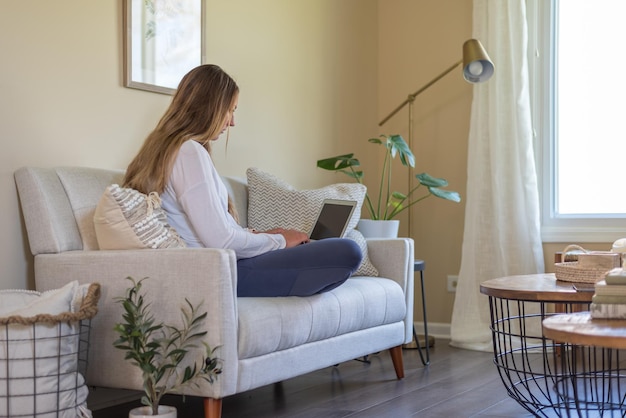 Mujer joven casual trabajando en una computadora portátil en casa en una sala de estar elegante