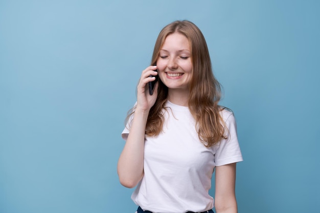 Mujer joven caucásica alegre hablando por teléfono sobre un fondo azul conexión móvil lindo sonriente gi...