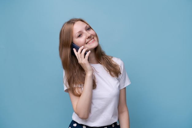 Mujer joven caucásica alegre hablando por teléfono sobre un fondo azul conexión móvil lindo sonriente gi...