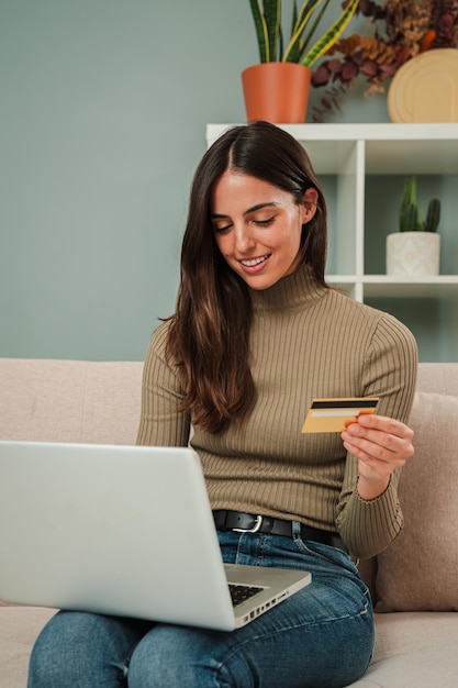 Mujer joven caucásica vertical usando una computadora portátil para hacer una compra en línea con una tarjeta de crédito sentada
