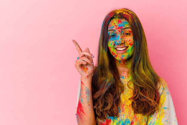 Mujer joven celebrando el festival sagrado aislado en la pared blanca sonriendo alegremente apuntando con el dedo índice lejos