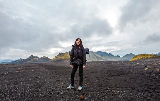 Una mujer joven en ceniza volcánica y una montaña verde. Landmannalaugar, Islandia