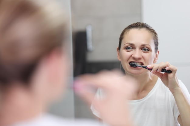 Mujer joven se cepilla los dientes en el baño delante del espejo