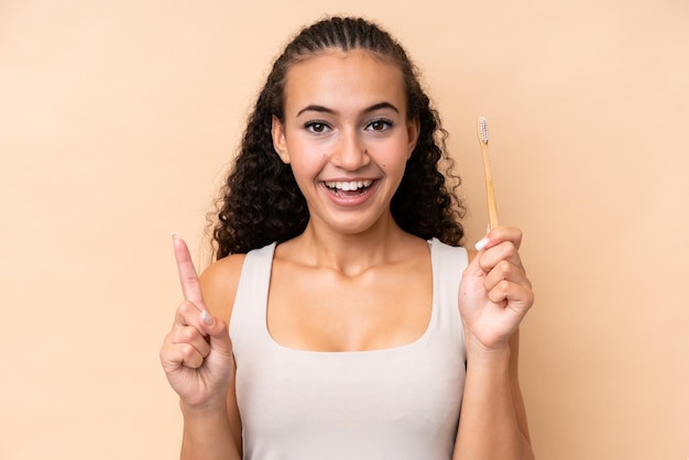 Mujer joven cepillando los dientes aislado sobre fondo beige señalando una gran idea