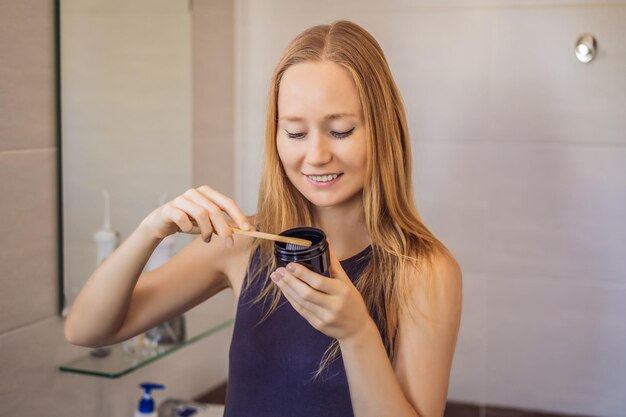 Mujer joven cepillándose los dientes con una pasta de dientes negra con carbón activo y cepillo de dientes negro