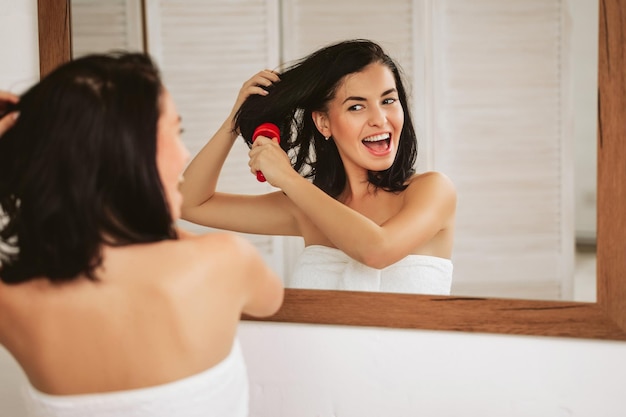 Mujer joven cepillarse el cabello sano delante de un espejo