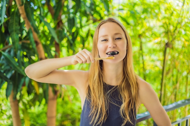 Mujer joven cepillarse los dientes con polvo de carbón activado para cepillarse y blanquearse los dientes Cepillo ecológico de bambú