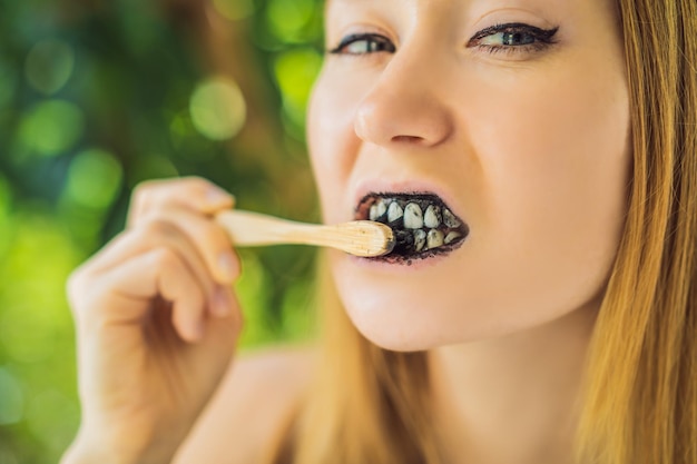 Mujer joven cepillarse los dientes con polvo de carbón activado para cepillarse y blanquearse los dientes Cepillo ecológico de bambú