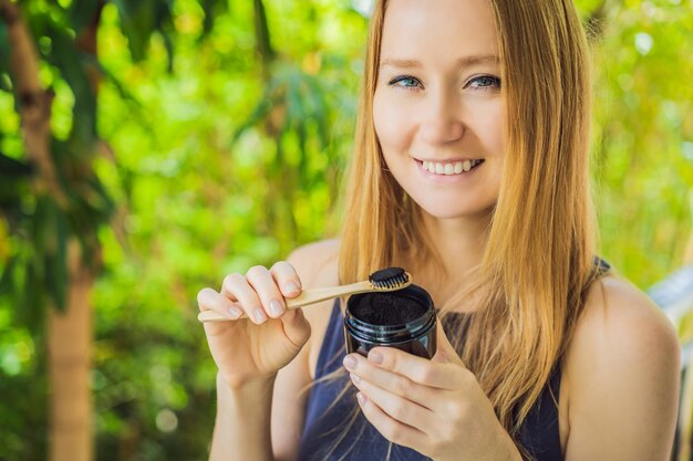 Mujer joven cepillarse los dientes con polvo de carbón activado para cepillarse y blanquearse los dientes Cepillo ecológico de bambú