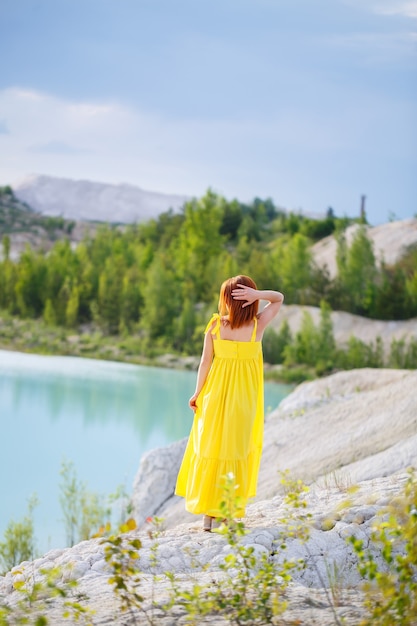 Mujer joven cerca de un lago con agua azul y montañas pedregosas con árboles verdes. Hermosa vista del lago en el bosque