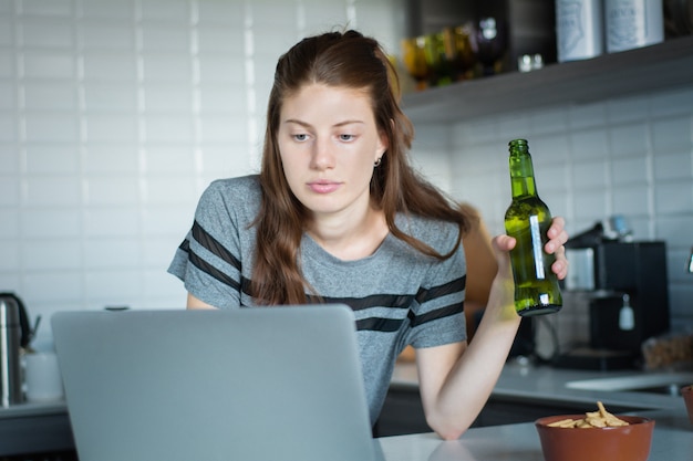 Mujer joven con cerveza y usando su laptop