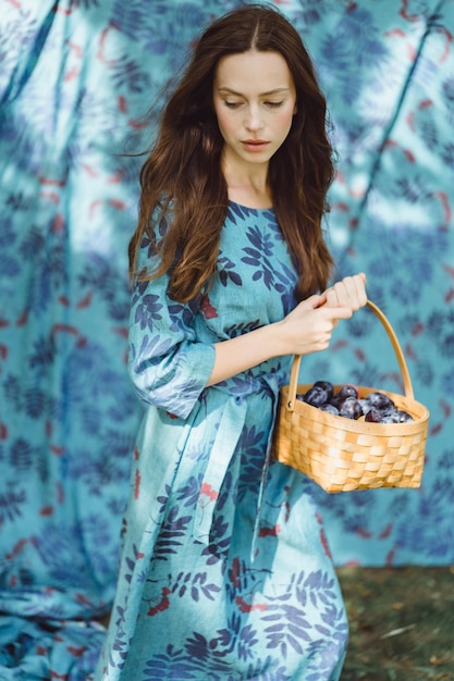 Foto mujer joven con una cesta de frutas, ciruelas y manzanas.