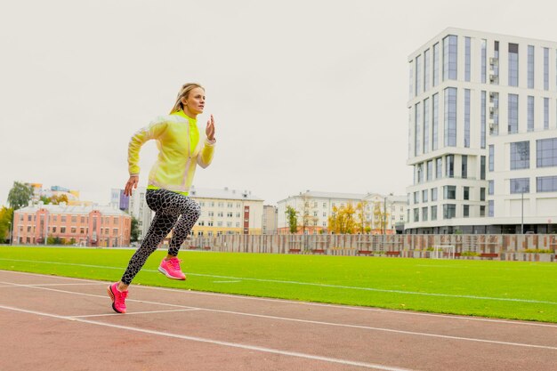 Una mujer joven con un chándal brillante corre en una cinta de correr en un estadio al aire libre