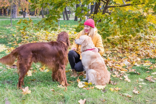 Mujer joven en una chaqueta abrigada con dos perros al aire libre en las hojas de otoño.