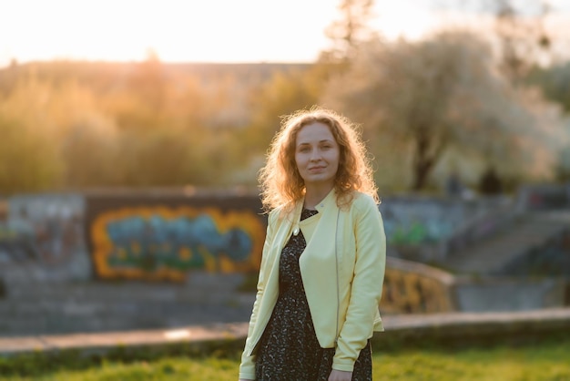 Una mujer joven con una chaqueta amarilla en el parque al atardecer.