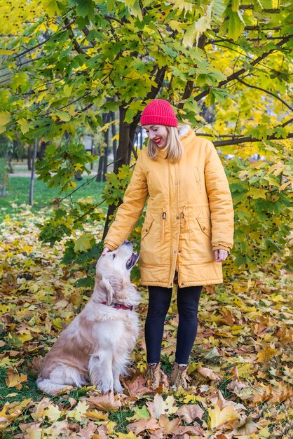 Mujer joven en una chaqueta amarilla con su perro perdiguero entre hojas de otoño amarillas