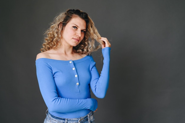 Foto mujer joven, en, chaqueta azul, es, tenencia, mechón de pelo, niña, acicalamiento, pelo rizado, mujer, en, pared gris