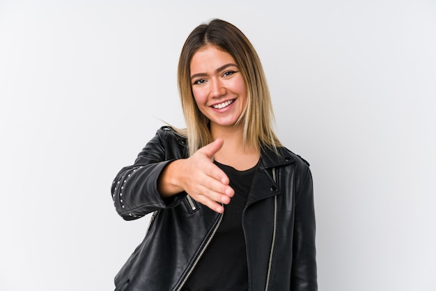 Mujer joven con una chaqueta de cuero negro estirando la mano a la cámara en gesto de saludo.