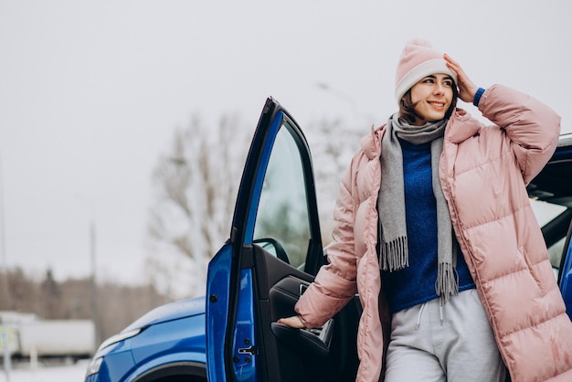 Mujer joven en chaqueta de invierno que se siente feliz por su nuevo auto azul