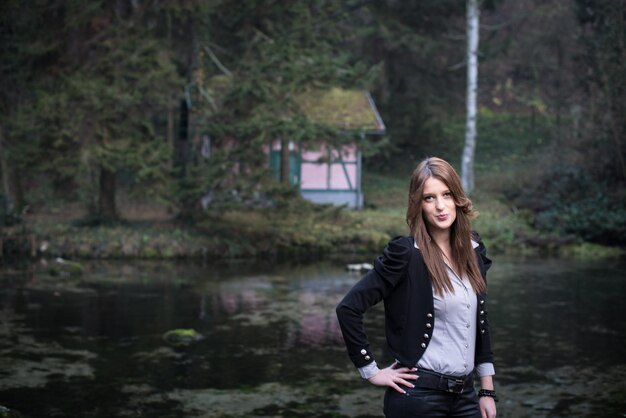 mujer joven en chaqueta de pie y posando en el lago