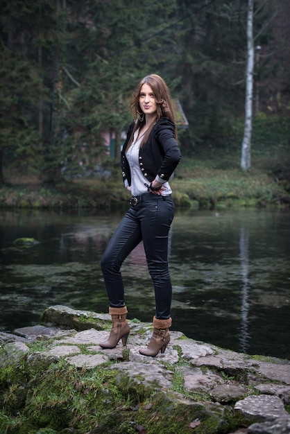 mujer joven en chaqueta de pie y posando en el lago