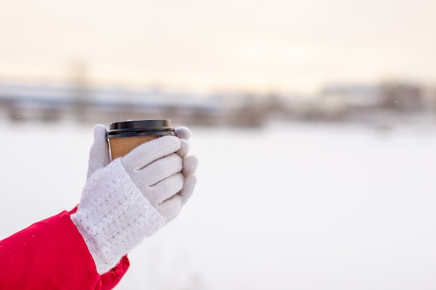 Una mujer joven con una chaqueta roja en invierno tiene un vaso de té o café caliente