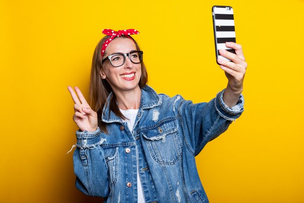 Mujer joven en una chaqueta vaquera y gafas sostiene un teléfono