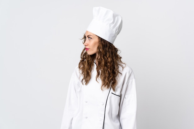 Mujer joven chef aislada en blanco mirando hacia el lado