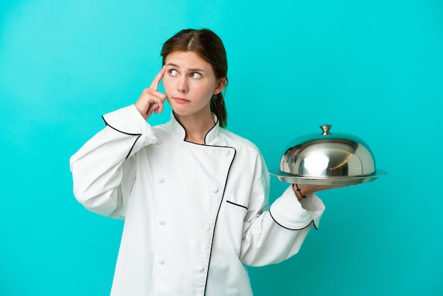 Mujer joven chef con bandeja aislada sobre fondo azul que tiene dudas y pensamiento