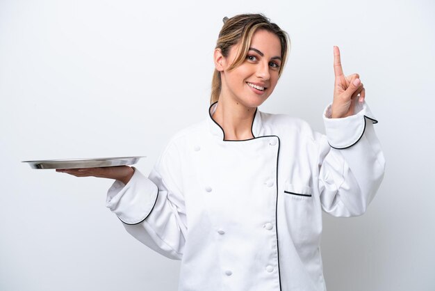 Mujer joven chef con bandeja aislada sobre fondo blanco mostrando y levantando un dedo en señal de lo mejor