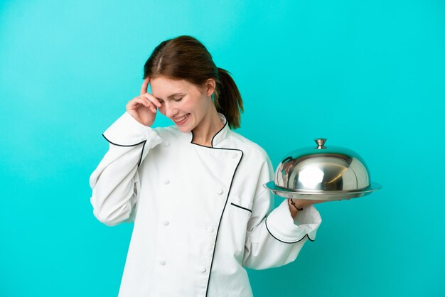 Mujer joven chef con bandeja aislado sobre fondo azul riendo
