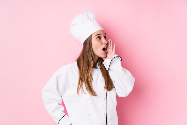 Mujer joven chef caucásica aislada gritando y sosteniendo la palma cerca de la boca abierta.